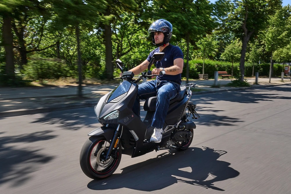Schwarzer Motorroller bei einer Fahrt auf einer sonnigen Straße